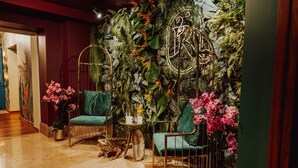 A room with a green sofa, a small round table with a vase of pink flowers, and a wall decorated with tropical plants and a neon sign. - Rezydencja Luxury Hotel & Wellness (Piekary Slaskie)