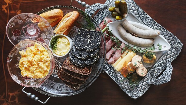 A variety of food items including bread, cheese, and sausages arranged on ornate silver trays.