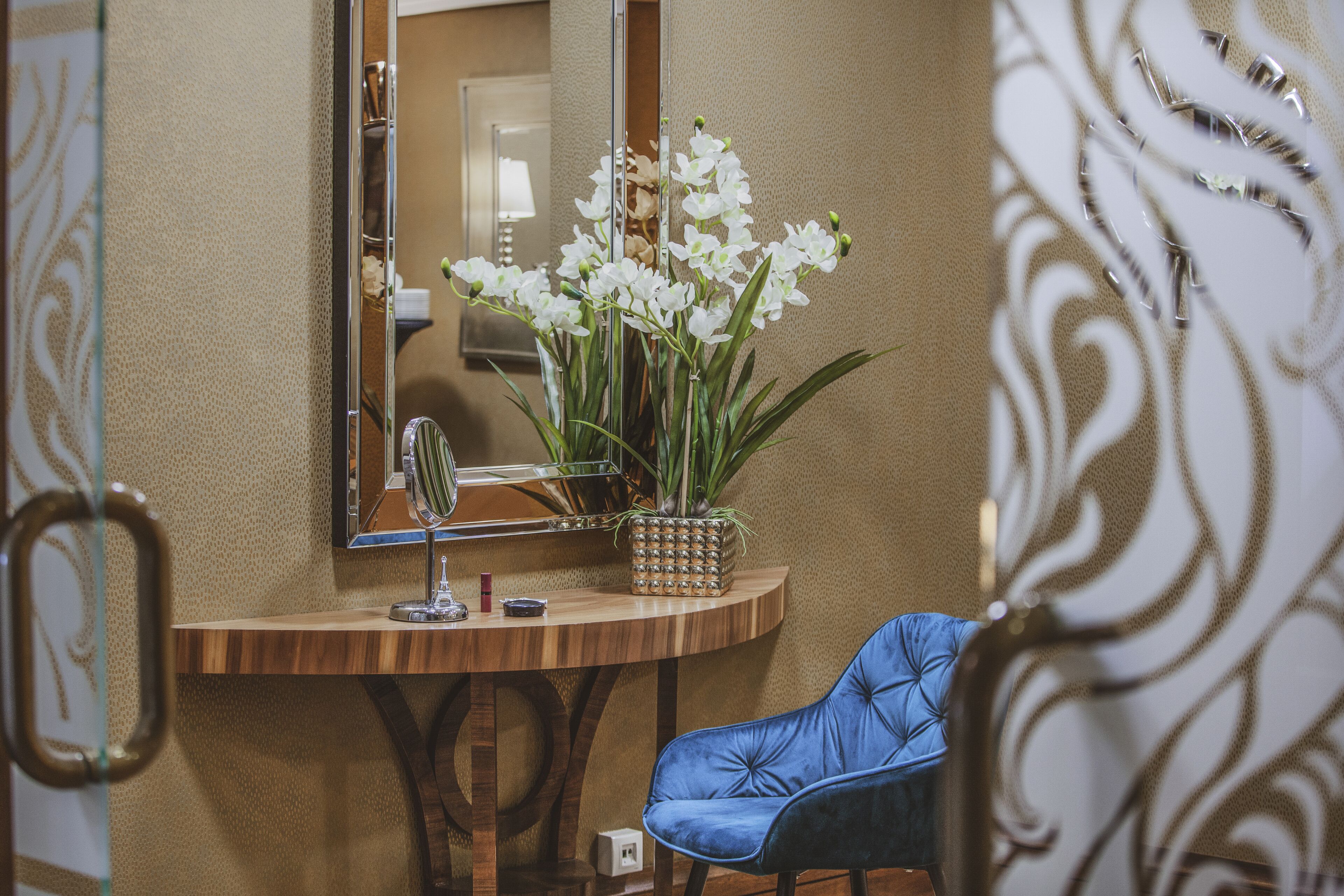A bathroom with a wooden vanity, a mirror, a blue chair, and a potted orchid plant.