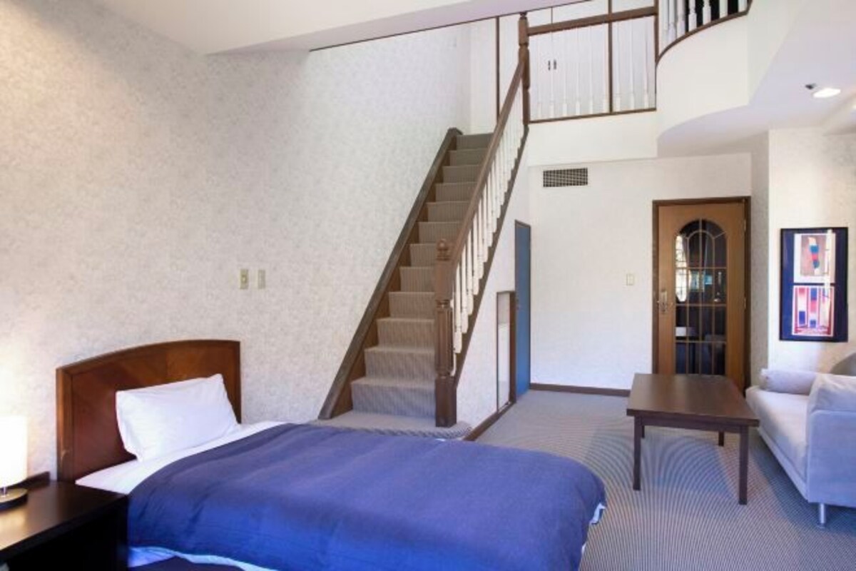 Una habitación de hotel con cama, escalera de madera, sofá y una pequeña mesa.