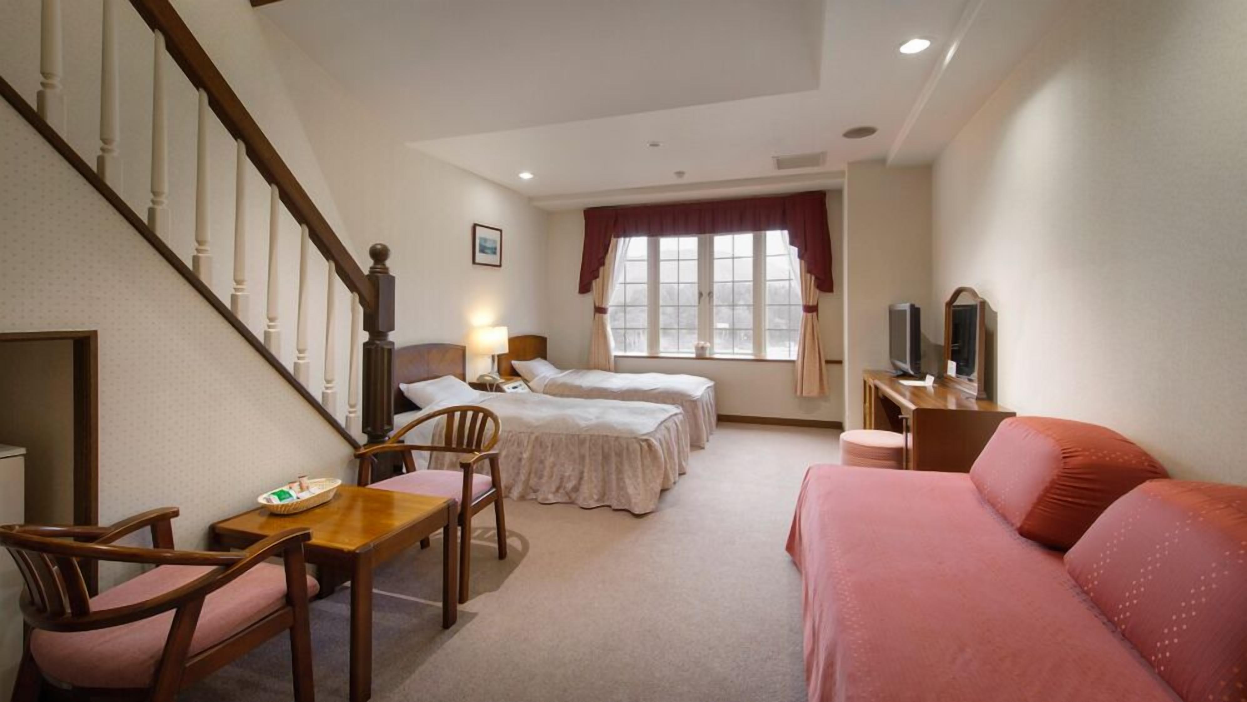 Quarto de hotel com escada, duas camas, uma escrivaninha com televisão e um sofá.