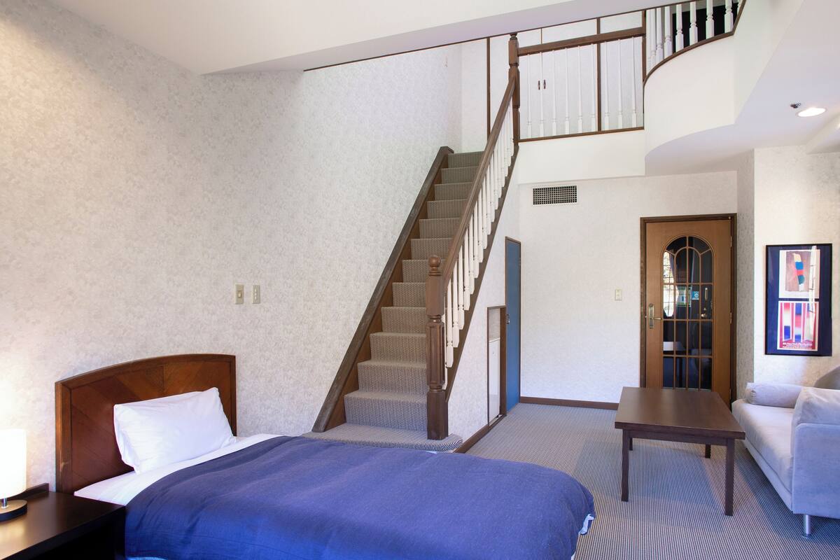Habitación de hotel con una cama grande, cabecera de madera, escritorio, silla, escalera y puerta.