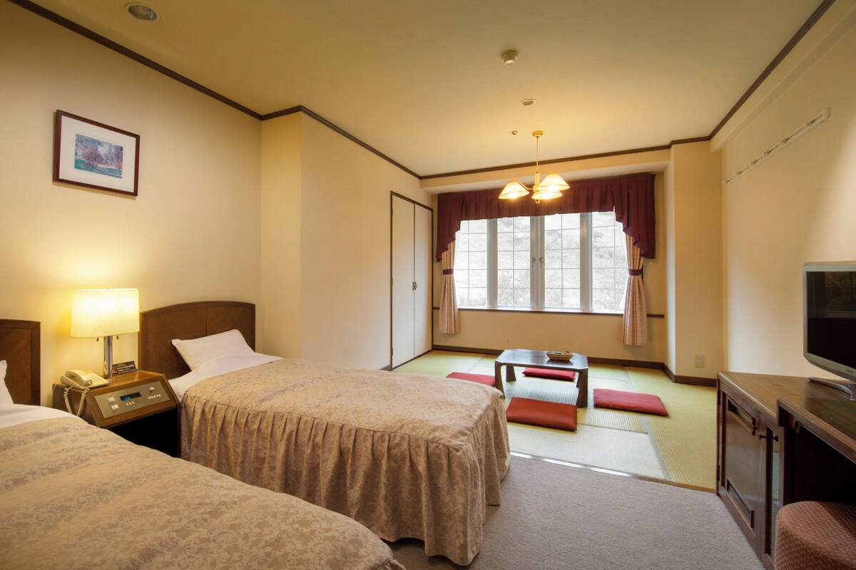 Una habitación de hotel con dos camas, un escritorio, un televisor y una ventana con cortinas.