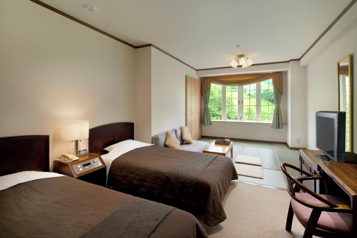 Una habitación de hotel con dos camas, un escritorio con silla, televisión y una ventana con cortinas.