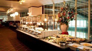 Ein reichhaltiges Buffet mit verschiedenen Speisestationen, einer großen Blumendekoration und einem modernen Innenraum mit großen Fenstern und Deckenleuchten.