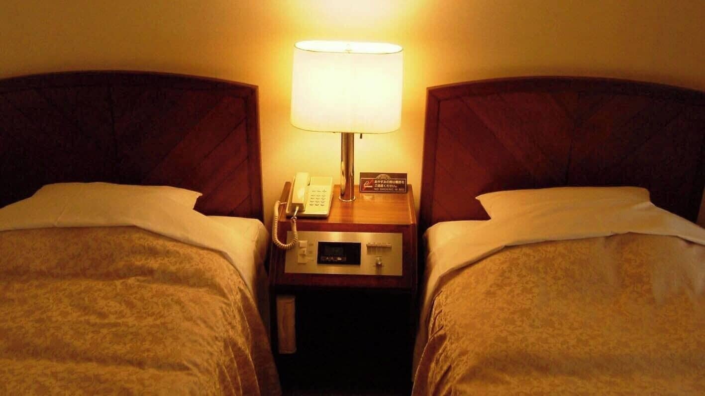 Habitación de hotel con dos camas, una lámpara de noche, un teléfono y un cartel con el número de la habitación.
