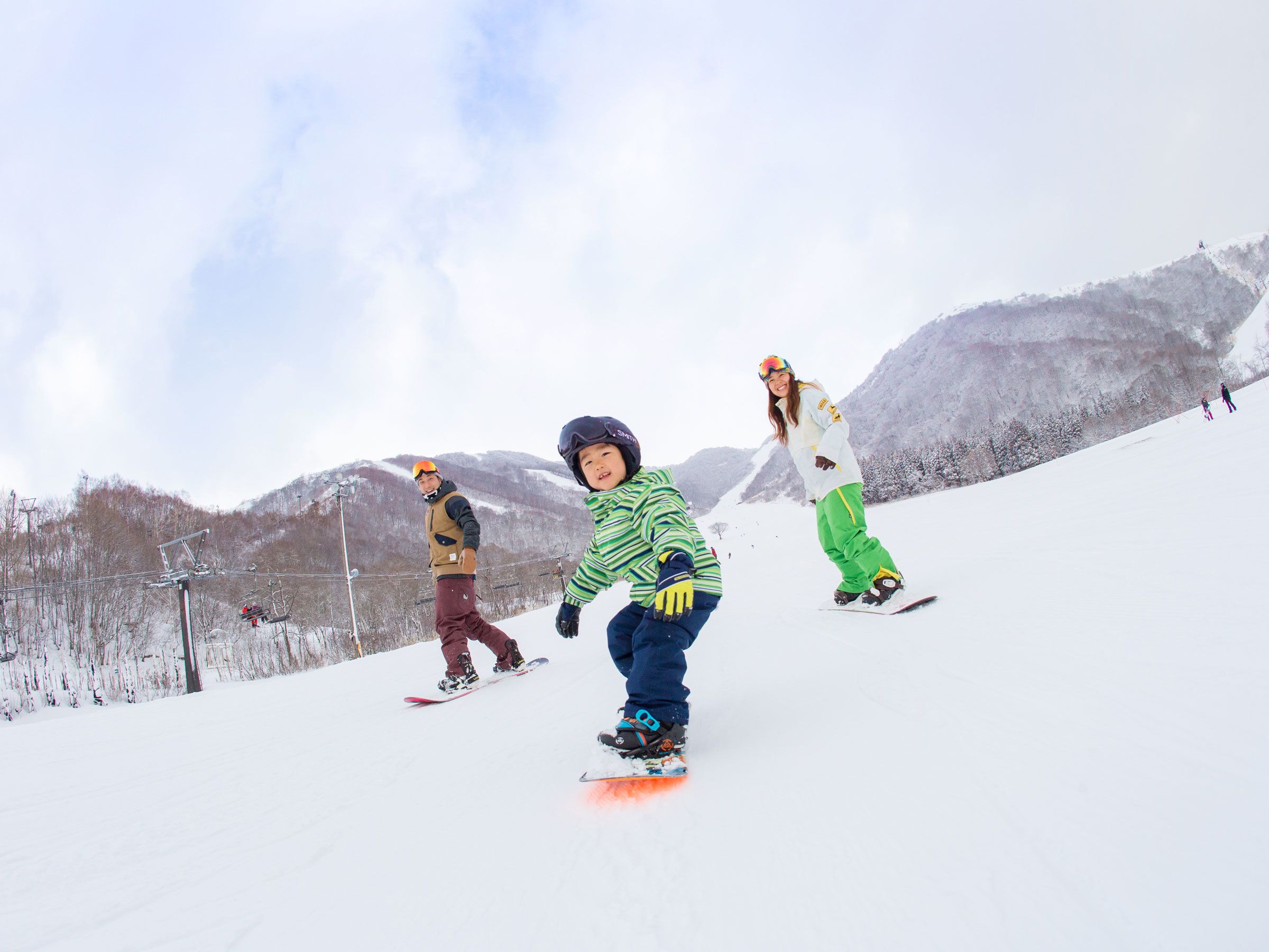 A snowy mountain slope with three individuals snowboarding.