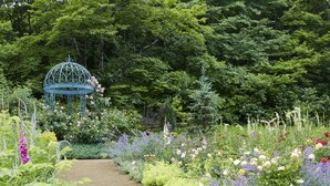 Ein Garten mit einem Gartenhaus, verschiedenen Blumen und einem Kiesweg.