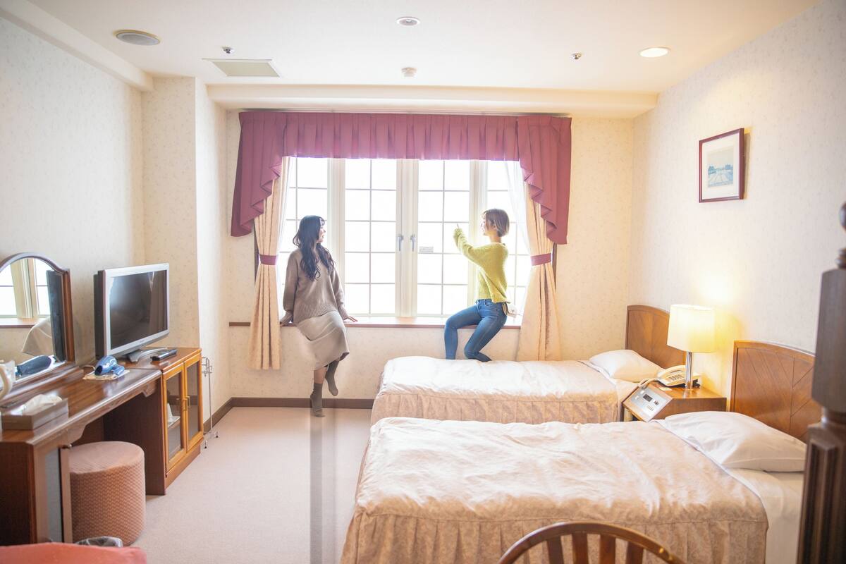 Habitación de hotel con dos camas, televisión, escritorio con ordenador y ventana con cortinas.