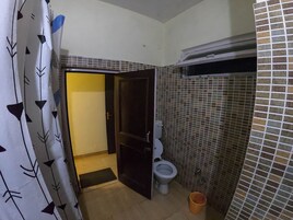 Un baño con inodoro, zona de ducha y pared con azulejos.