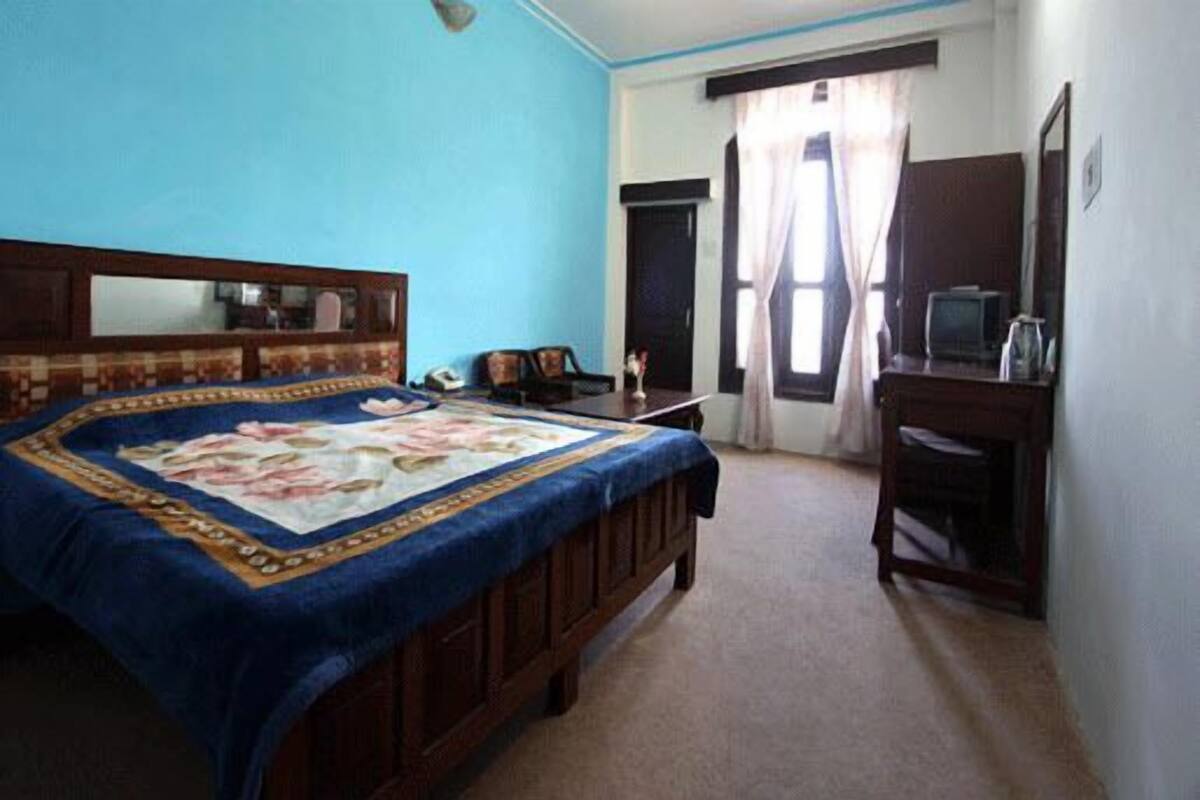 A bedroom with a bed, a desk, a chair, a television, and a window with curtains.