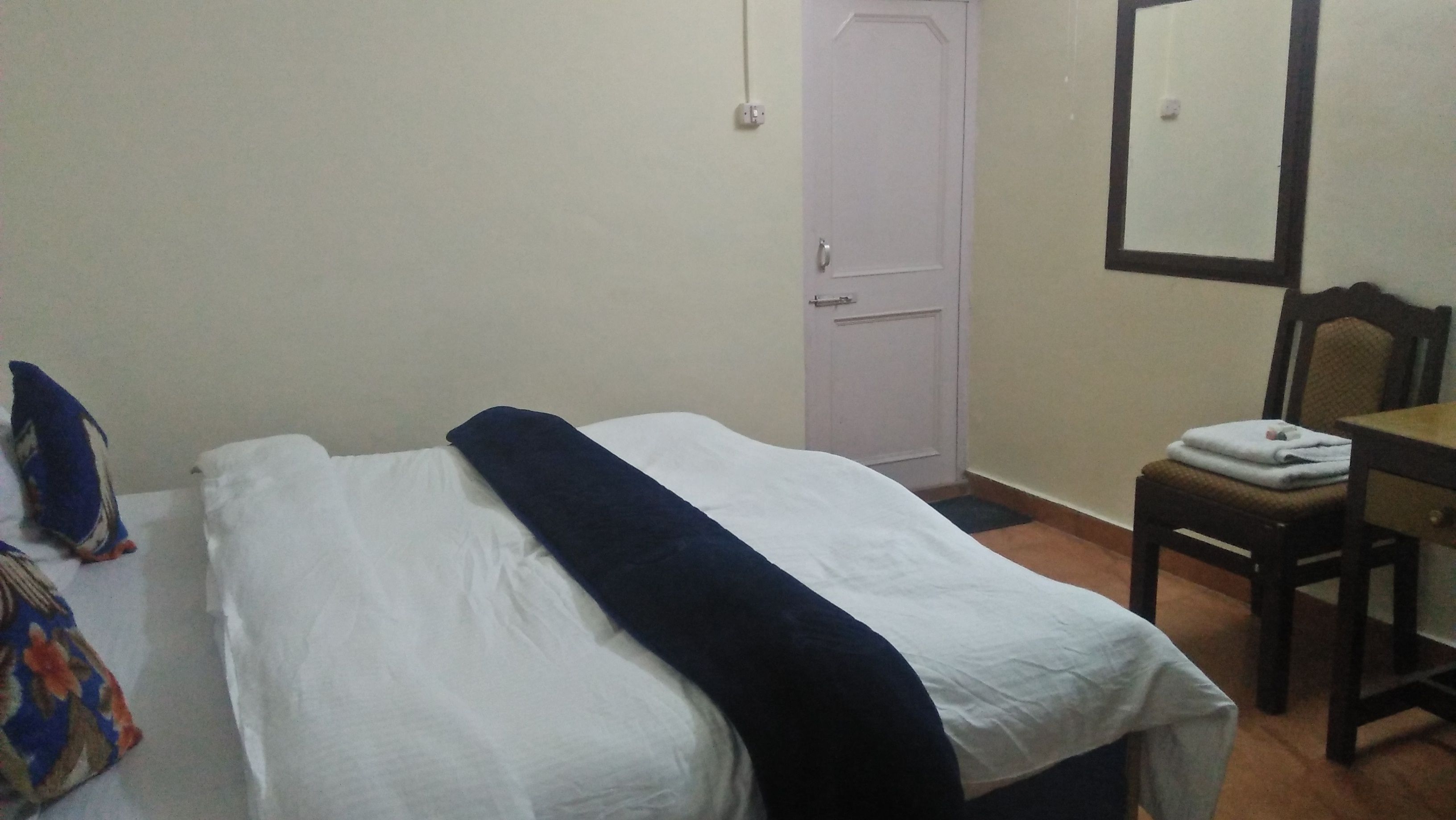 A simple room with a bed, a chair, a desk, and a door.