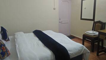 A simple room with a bed, a chair, a desk, and a door.
