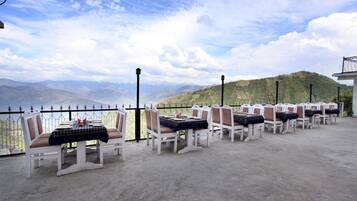 A terrace with white chairs and tables, overlooking a mountainous landscape.
