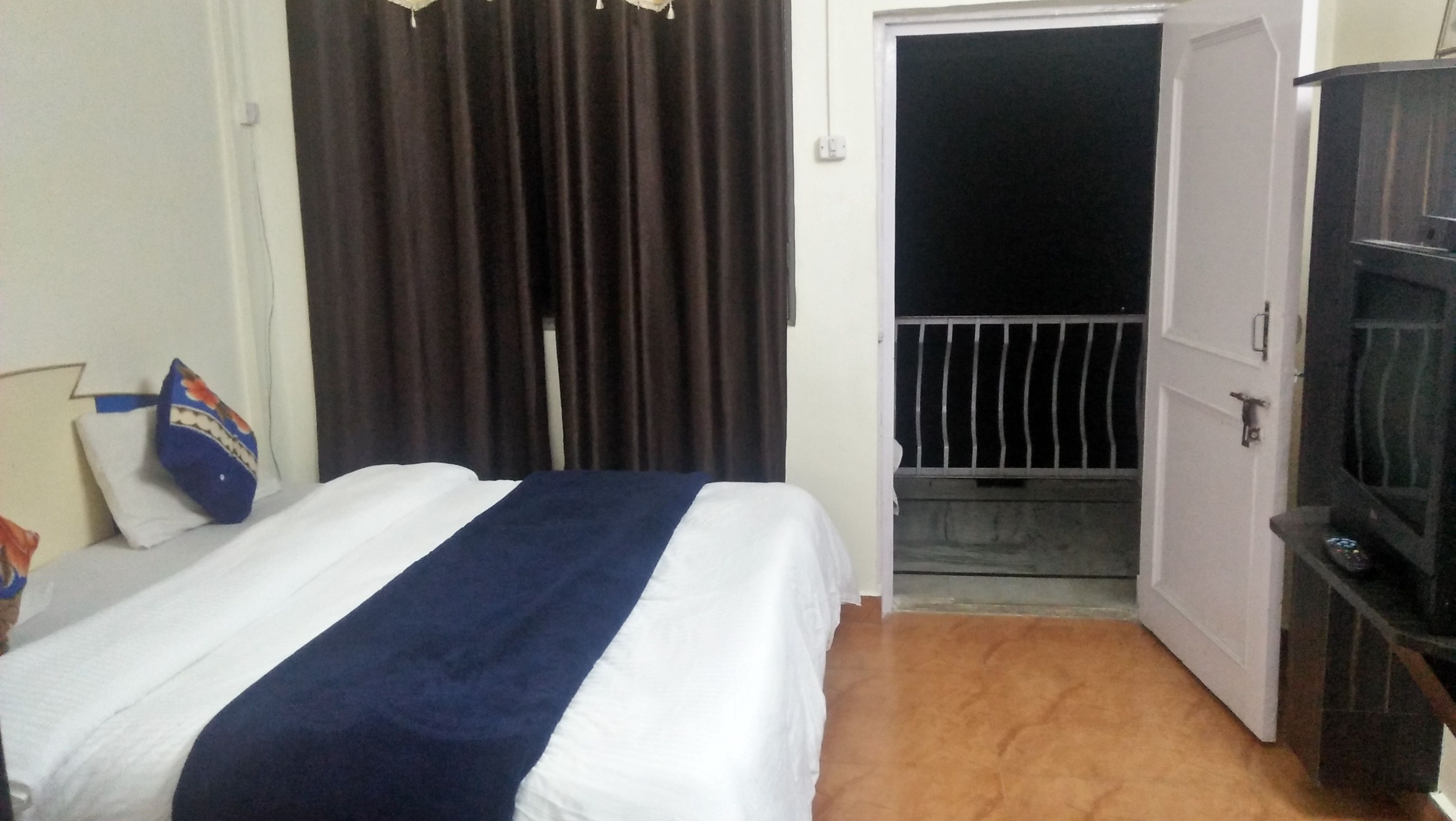 A hotel room with a bed, a TV stand, and a door leading to a balcony.