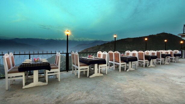 A terrace with tables and chairs, overlooking a mountainous landscape. - Shining Star Resort (Chamba)