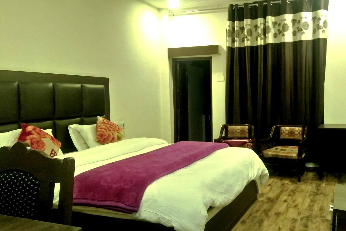 A hotel room with a bed, two chairs, a TV, and a door.