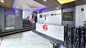 A modern reception area with a marble reception desk, a Coca-Cola refrigerator, a staircase, and a wall-mounted clock. - Shining Star Resort (Chamba)