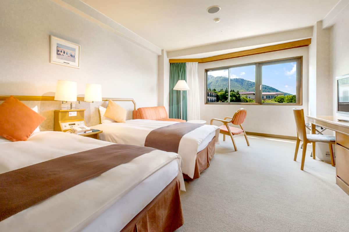 Ein Hotelzimmer mit zwei Betten, einem Schreibtisch, einem Stuhl und einem Fenster mit Blick auf die Berge.