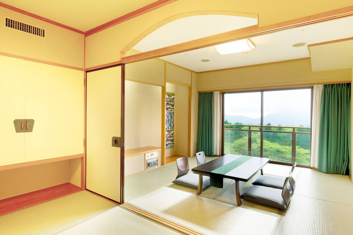 Ein traditioneller japanischer Raum mit Tatami-Böden, einem niedrigen Tisch und Blick auf Grün durch große Fenster.