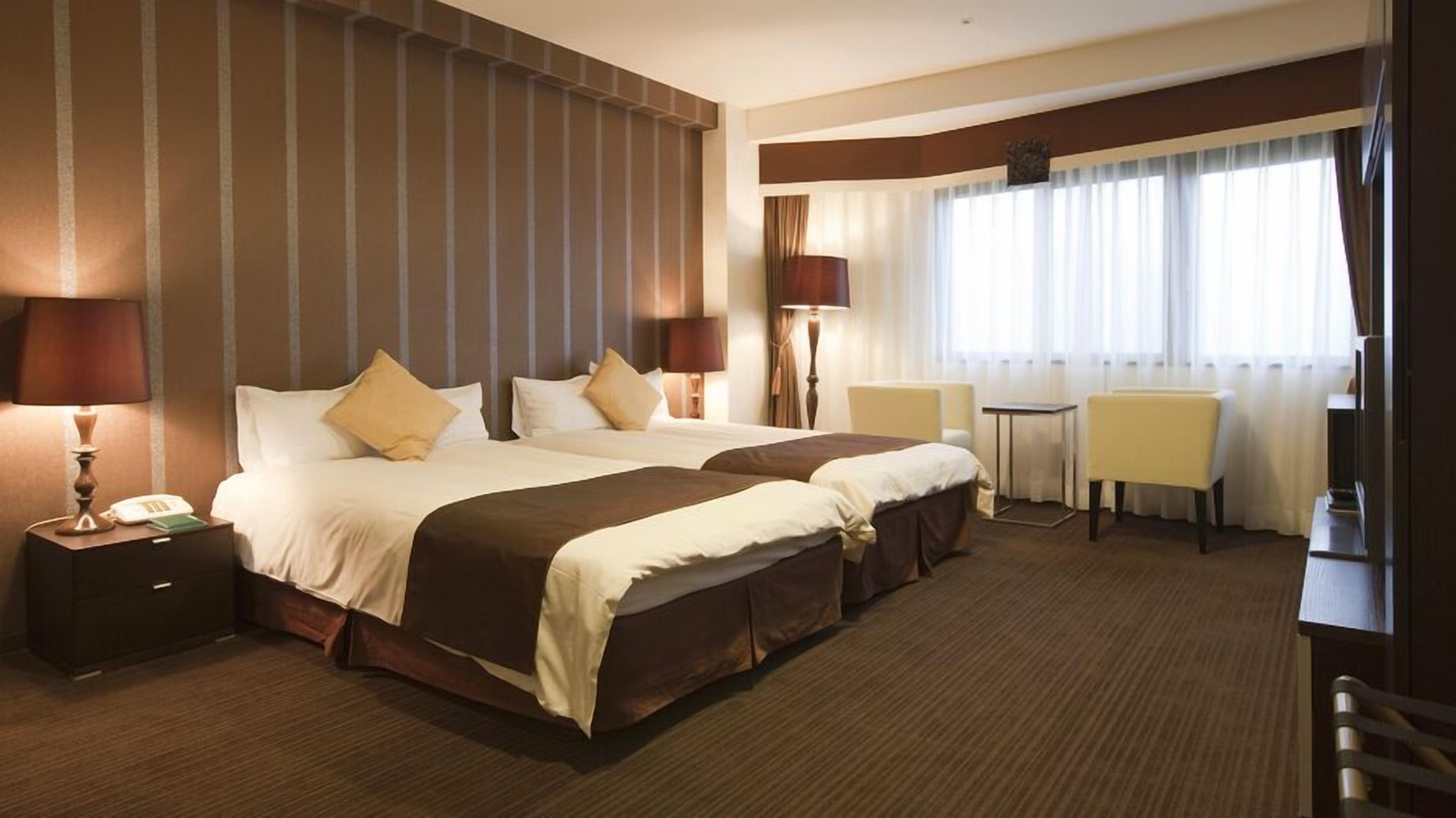 Une chambre d’hôtel avec deux lits, un bureau, des chaises et une grande fenêtre avec des rideaux.