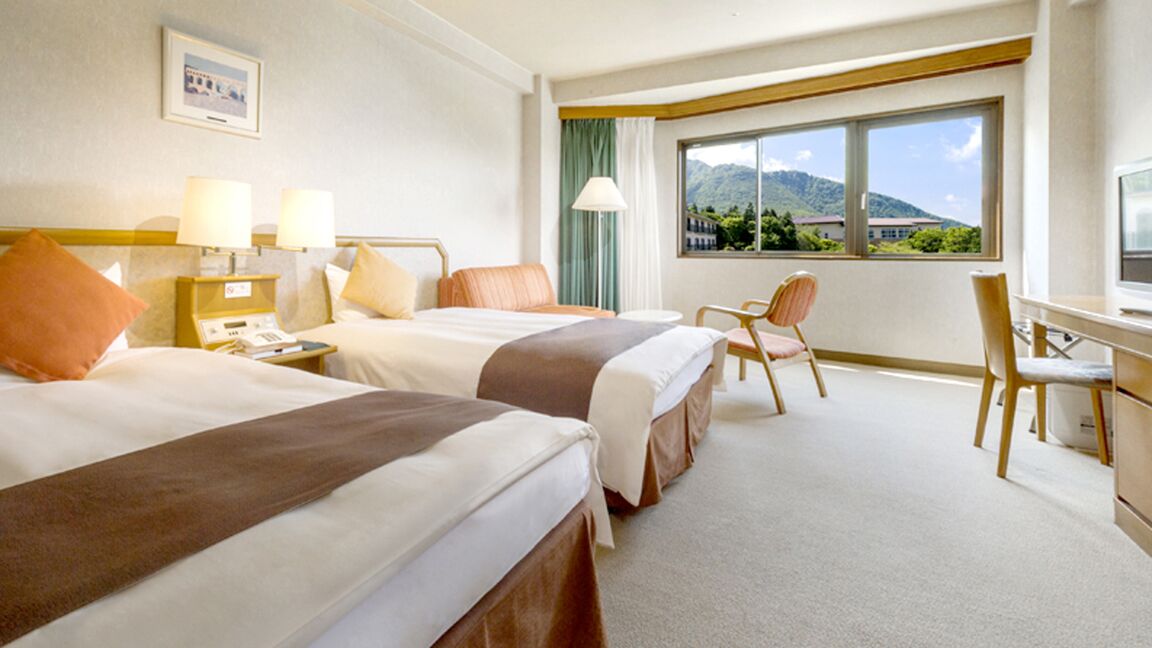 Une chambre d’hôtel avec deux lits, un bureau, une chaise et une grande fenêtre donnant sur la montagne.