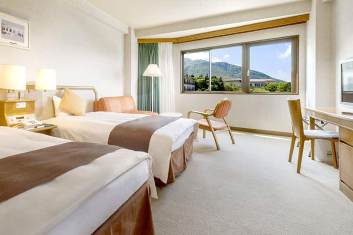 Ein Hotelzimmer mit zwei Betten, einem Schreibtisch, einem Stuhl und einem großen Fenster mit Blick auf die Berge.
