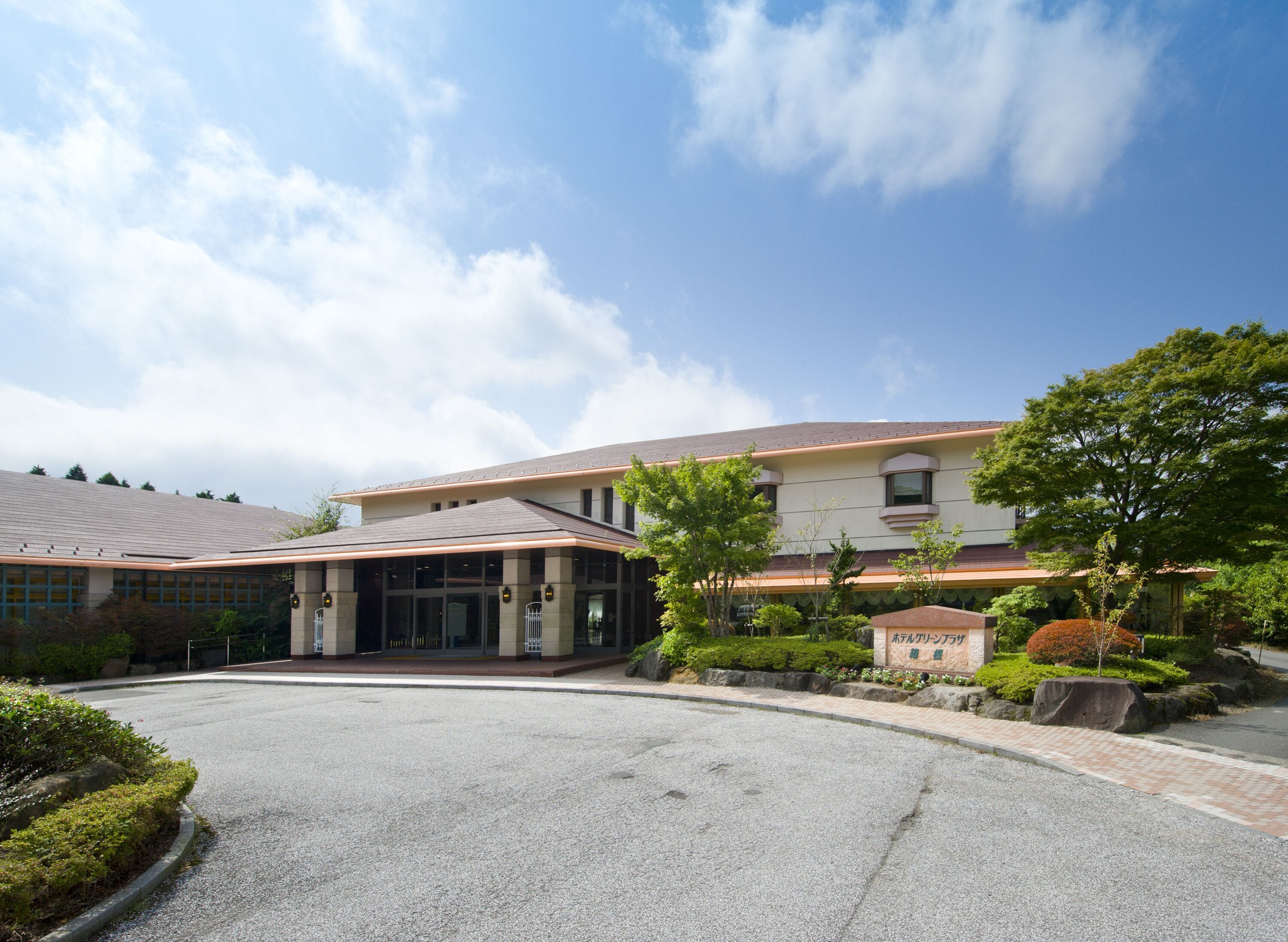 A building with a covered entrance, a parking area, and landscaped gardens.