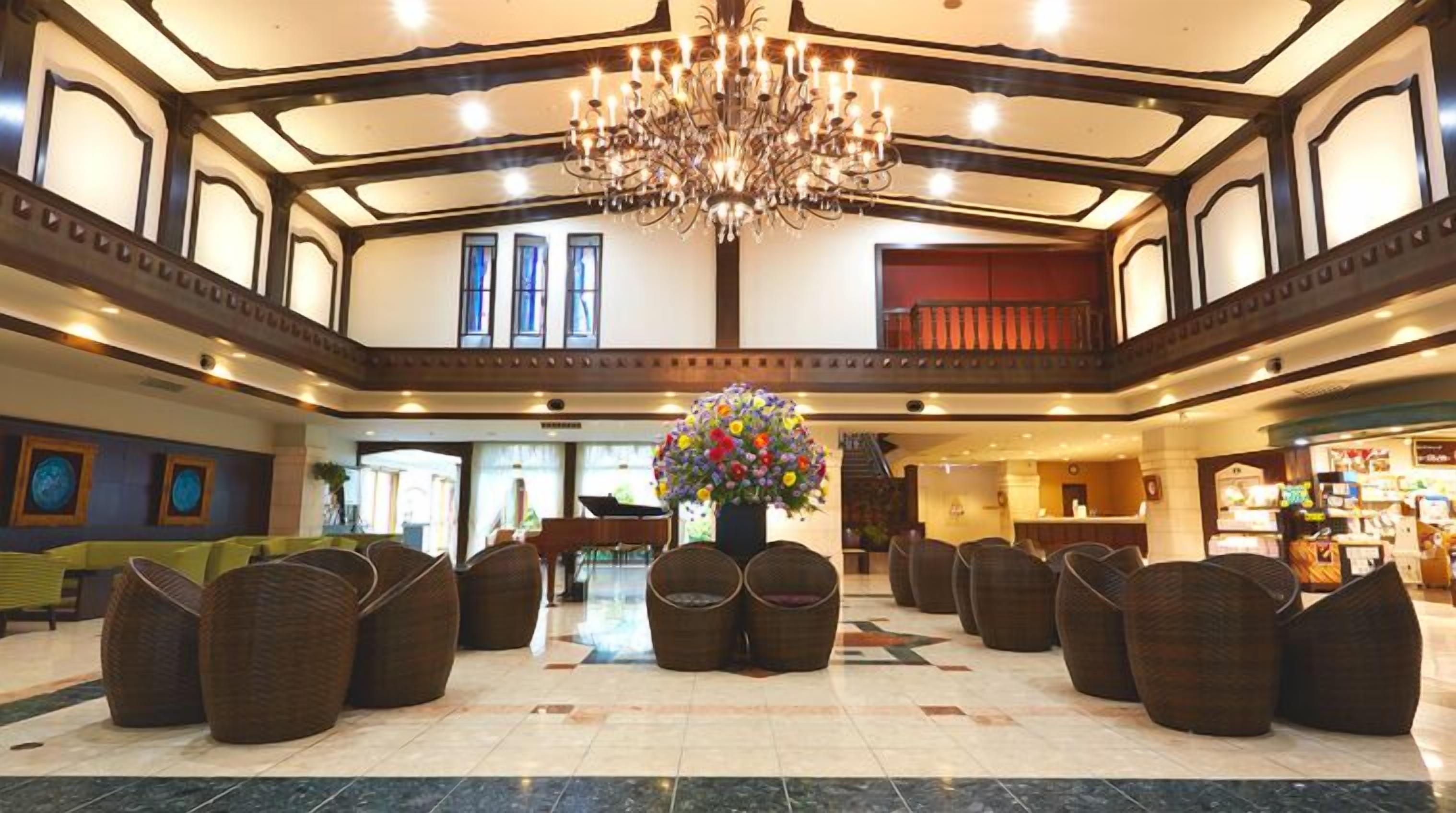 Um hall amplo com um lustre grande, assentos de vime e um arranjo floral central.