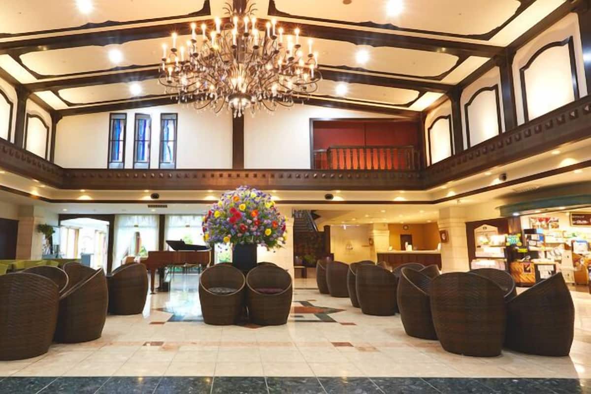 Eine geräumige Lobby mit einem großen Kronleuchter, Korbmöbeln und einer zentralen Blumenkomposition.