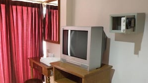 A room with a wooden desk, a television on top, a small refrigerator, and a mirror on the wall.