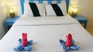 A double bed with white and green pillows, two blue nightstands with lamps, and towels folded on the bed.