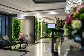 Een hal met een groene wand, moderne stoelen, een receptiebalie en een kroonluchter.