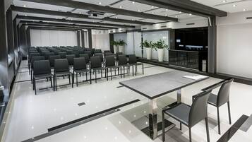 Una sala de conferències moderna amb files de cadires, una taula de vidre i una pantalla gran.