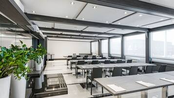 Una sala de conferencias moderna con paredes de vidrio, varias mesas y sillas, y un diseño limpio y minimalista.