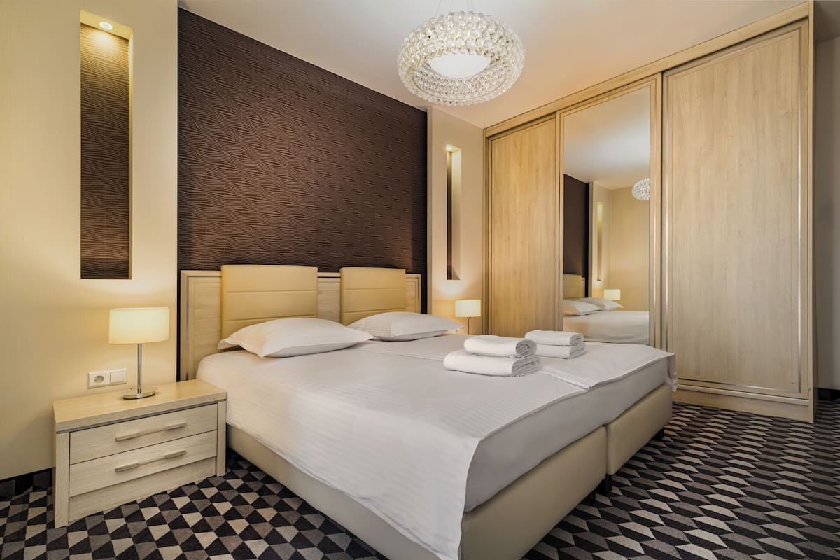 Quarto de hotel com uma cama grande, uma mesa de cabeceira com abajur, um espelho e um chão estampado.