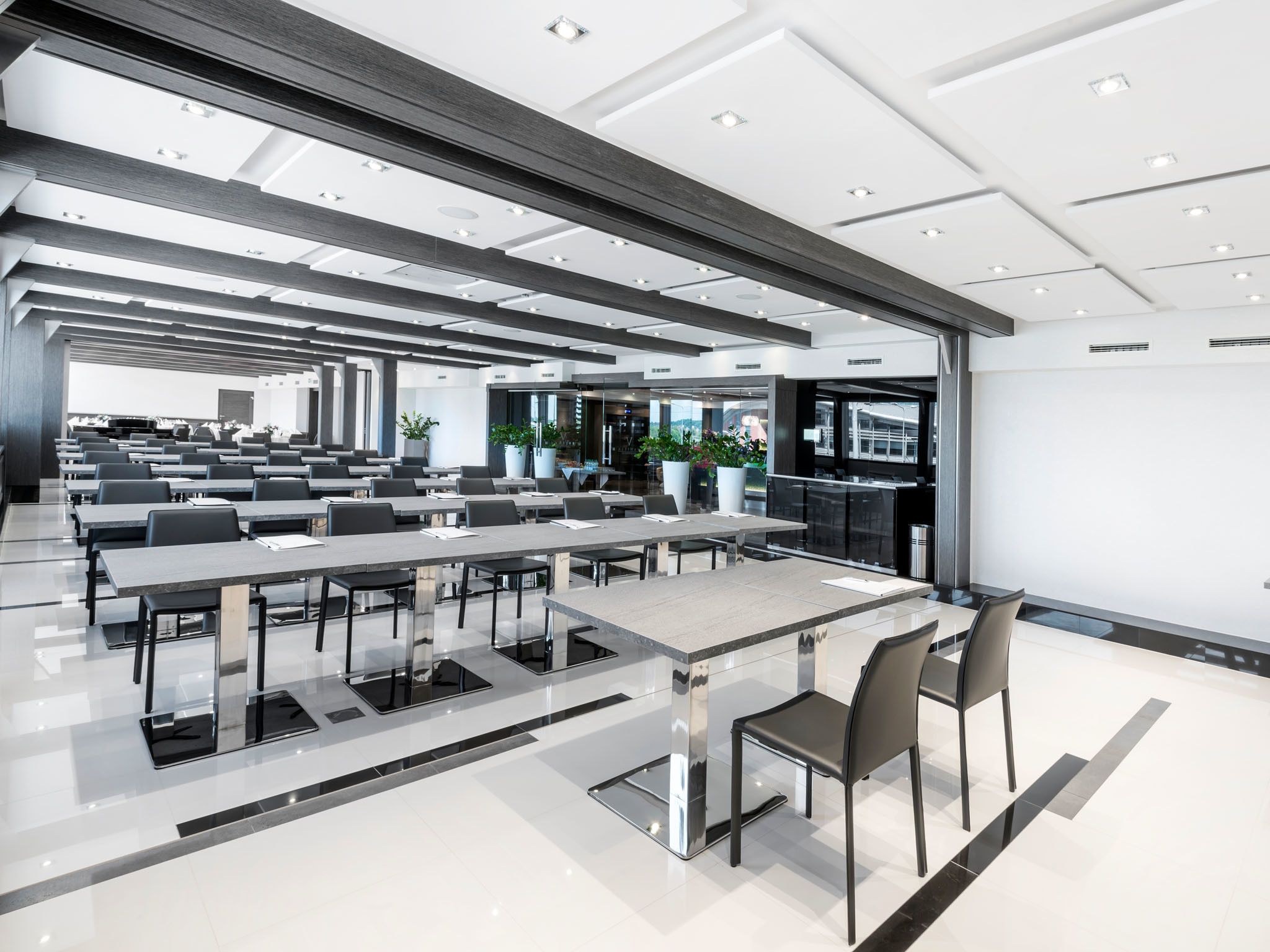 Une salle de conférence moderne, dotée de longues tables, de chaises et d’une cloison en verre.