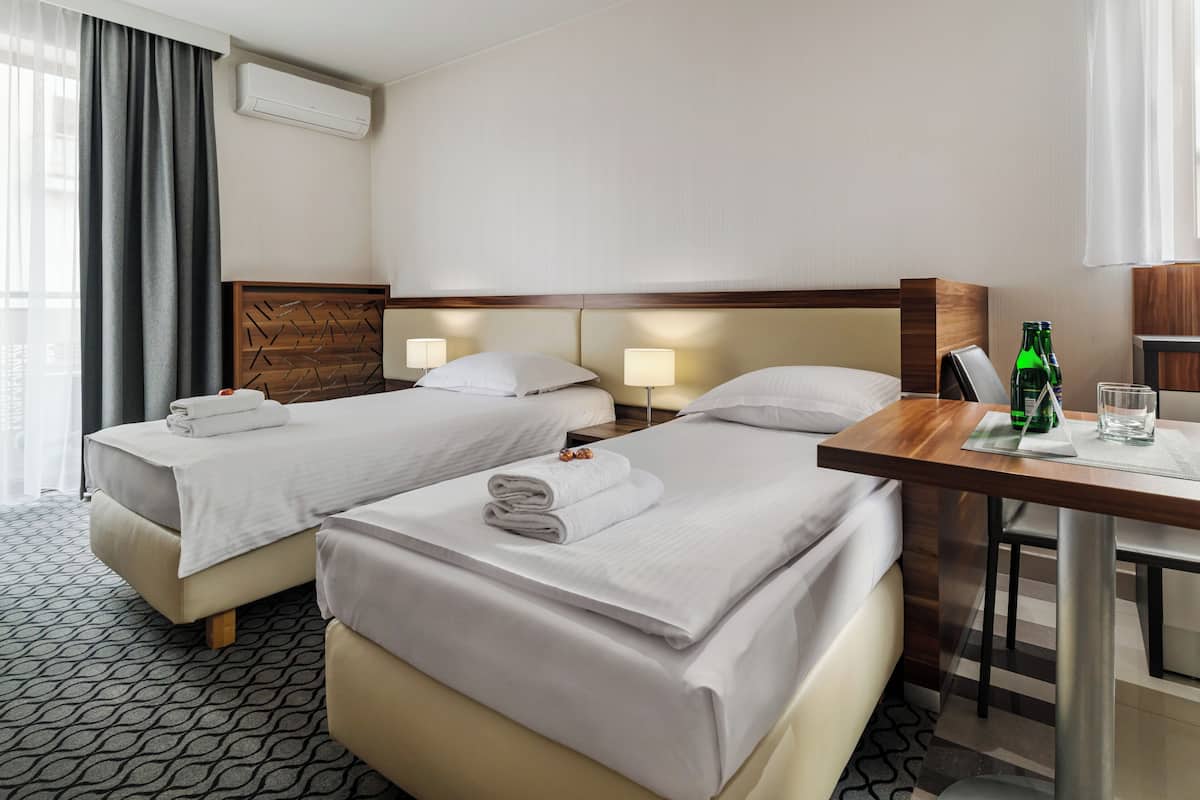 Quarto de hotel com duas camas, uma mesa e uma cadeira.