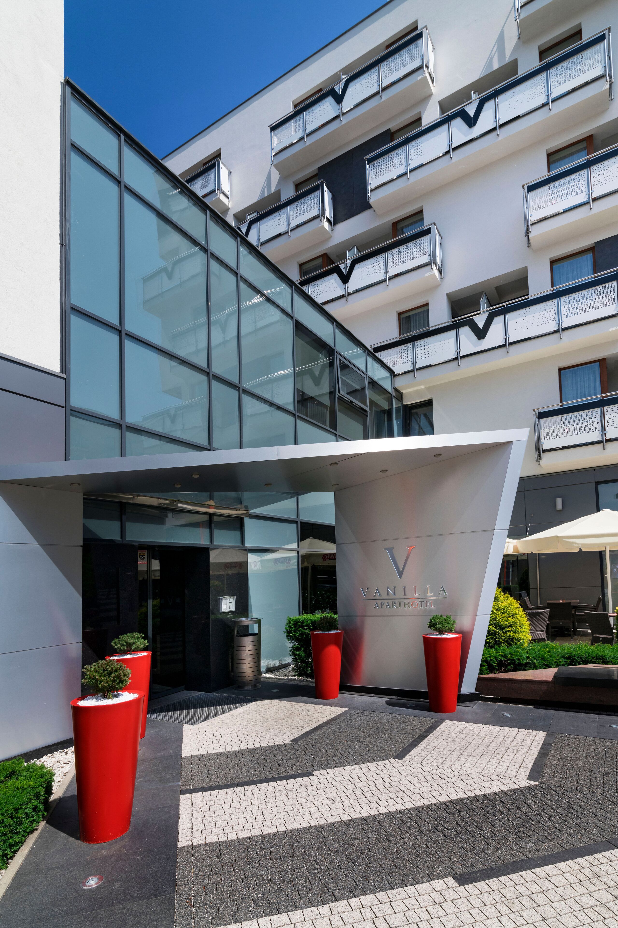 Edifici modern amb façana de vidre, un rètol que diu “Vanilla Apartments” i testos vermells amb petits arbres.