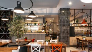 A restaurant interior with wooden tables, chairs, pendant lighting, a bar area, and a potted plant. - Vanilla Aparthotel (Kraków)