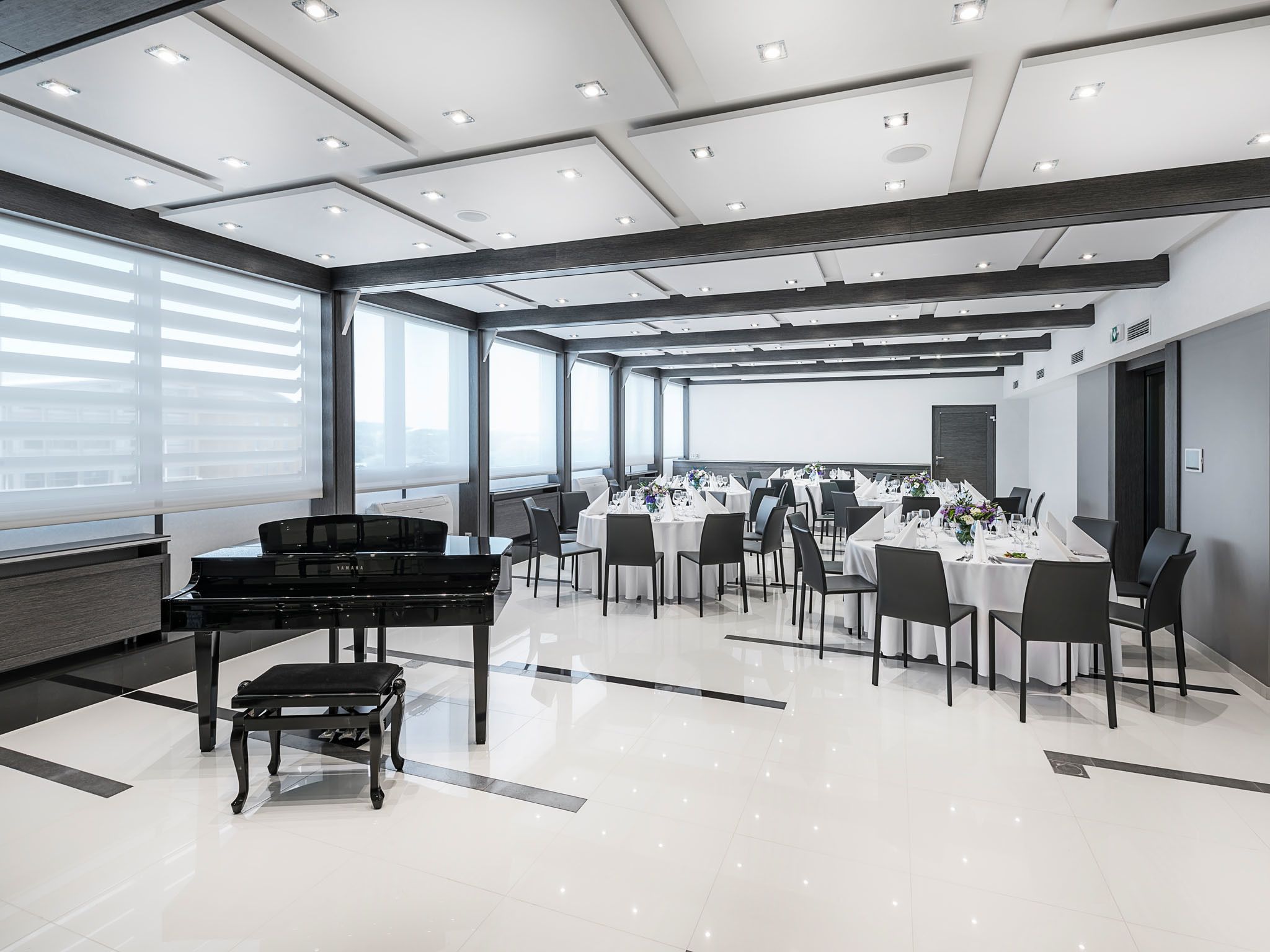Una sala de conferencias moderna con un piano, mesas redondas y sillas.