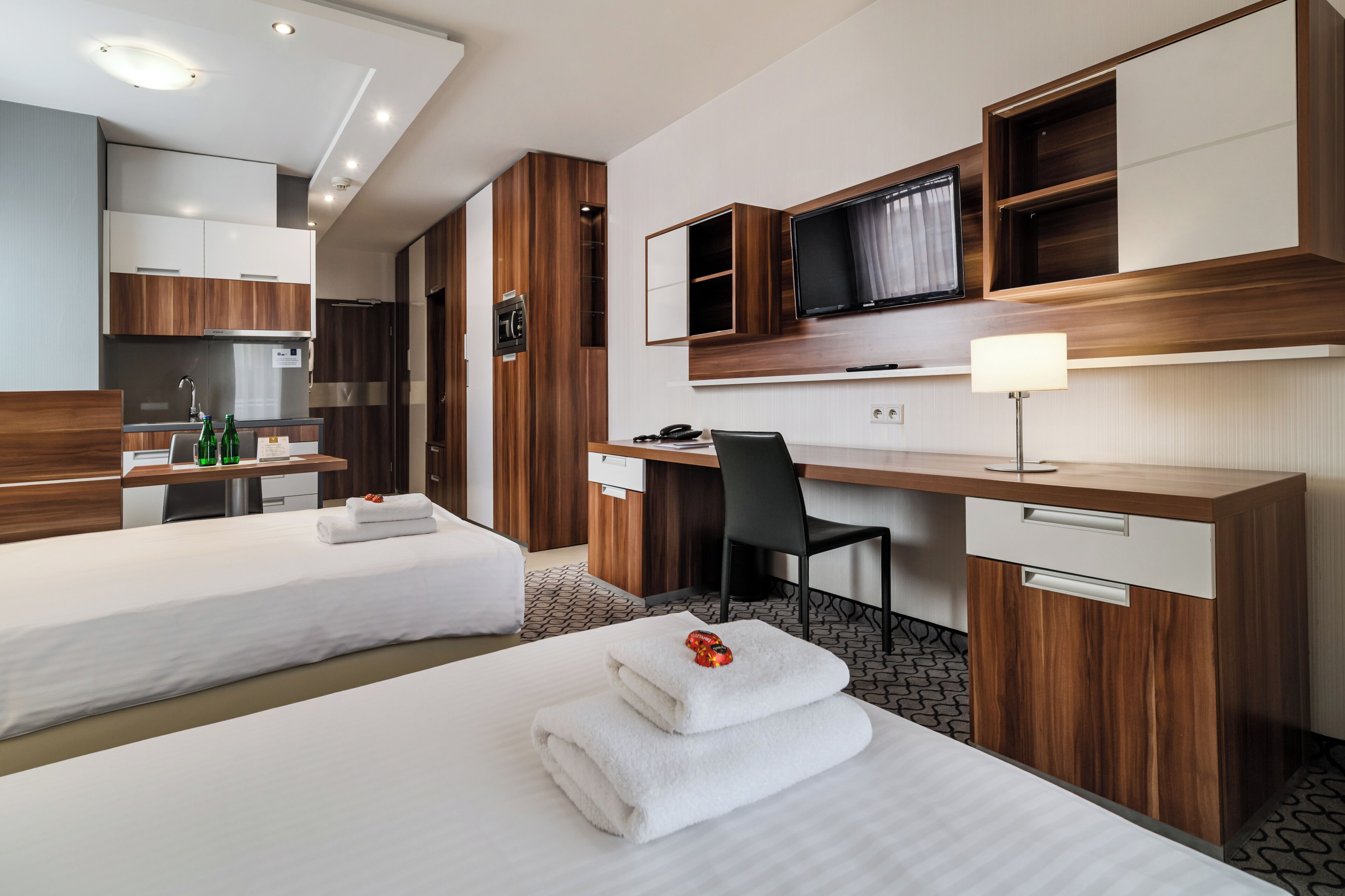 Une chambre d’hôtel avec deux lits, un bureau, une chaise, une télévision et un mini-bar.