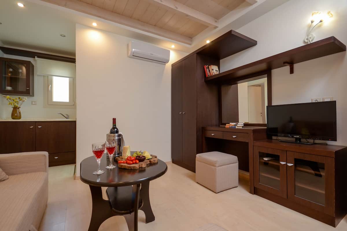 A modern living room with a round table, a sofa, a TV, and a kitchen area with cabinets and an air conditioner.