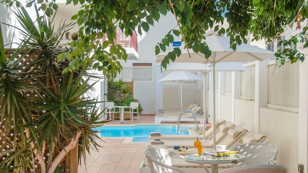 A poolside area with lounge chairs and a table, surrounded by greenery and a pool. - Aeolis Boutique Hotel (Naxos)