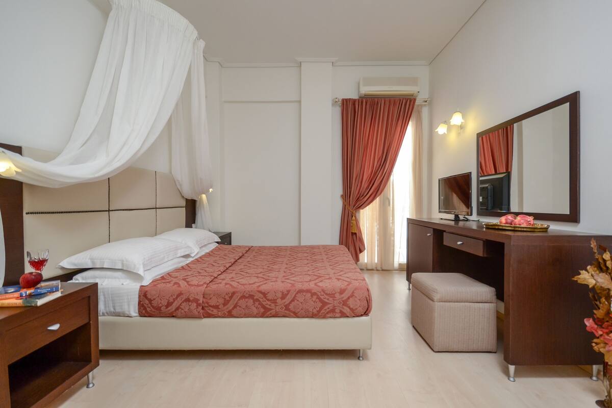 A bedroom with a bed, bedside table, vanity, and a mirror.