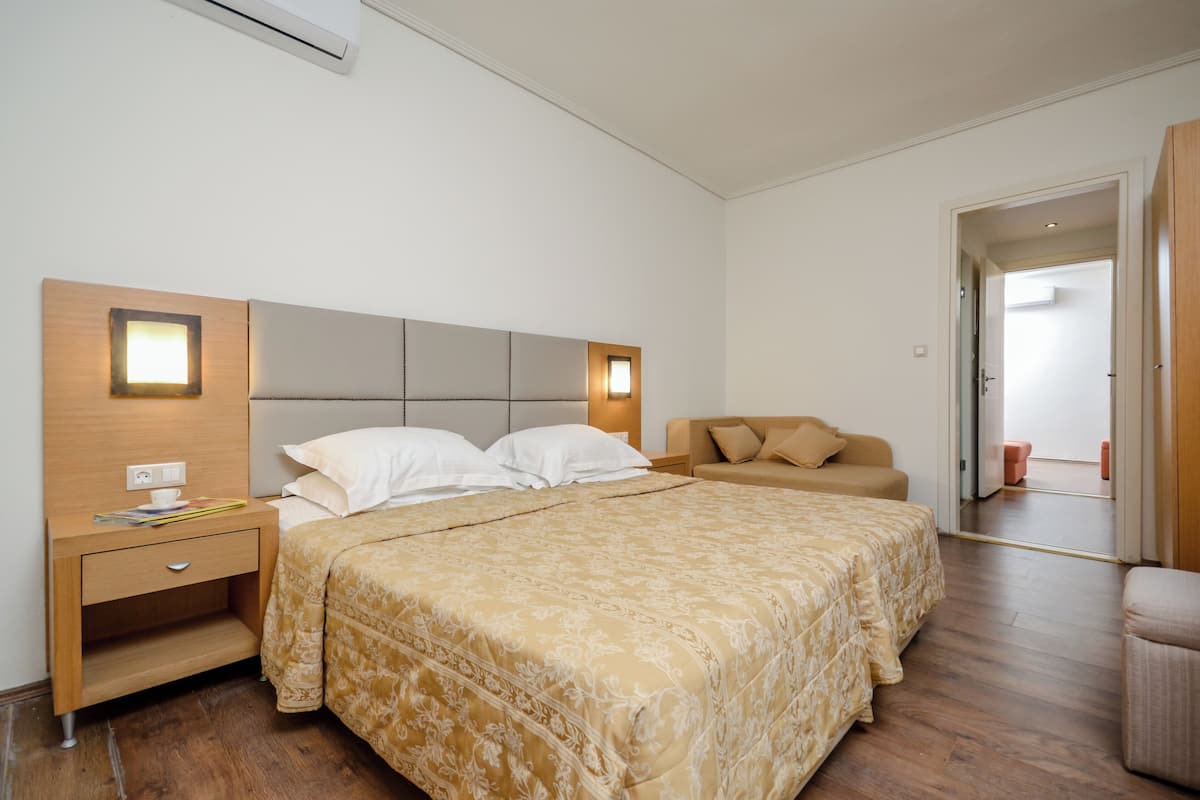 A bedroom with a large bed, a nightstand, a sofa, and a door leading to another room.