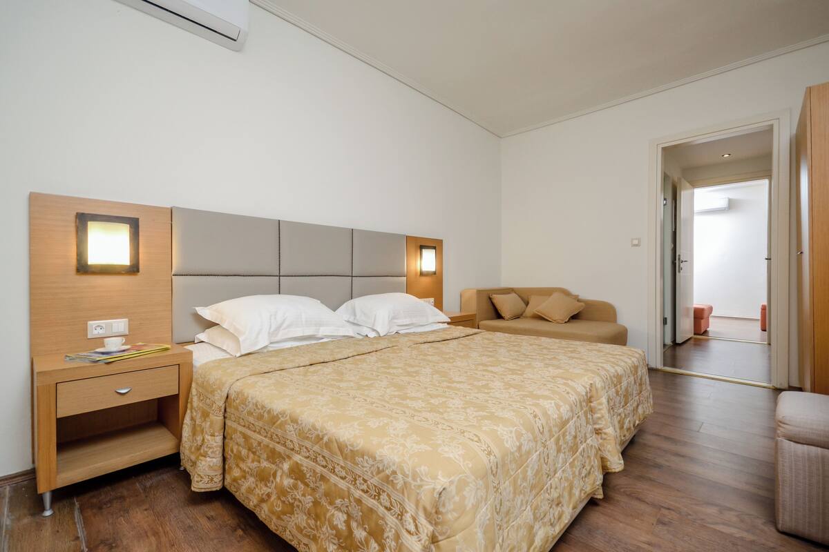 A bedroom with a bed, bedside table, nightstand, and a door leading to another room.