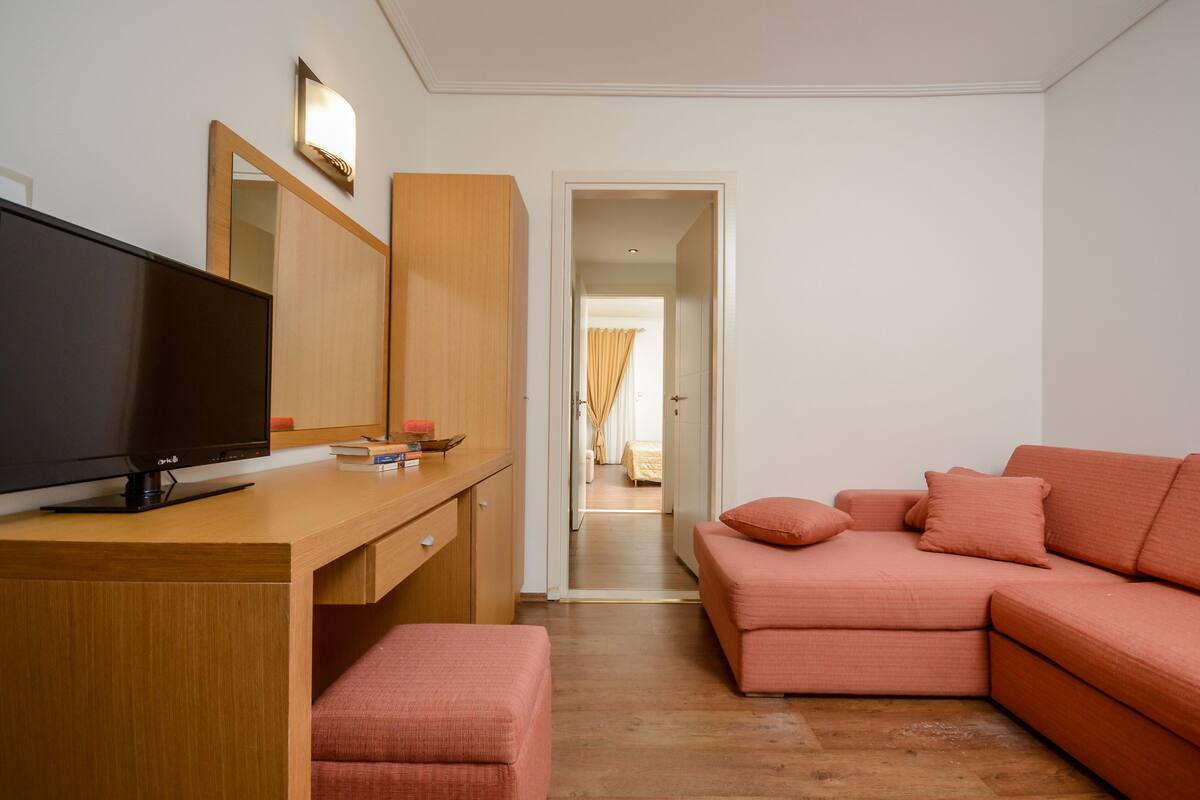 A room with a wooden desk, a television, a pink sofa, and a mirror.