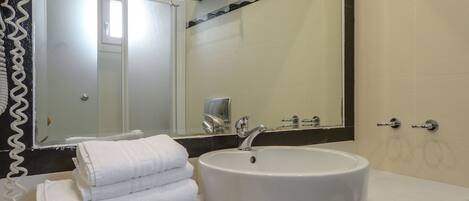 Une salle de bain avec un lavabo blanc, un grand miroir et un porte-serviettes.