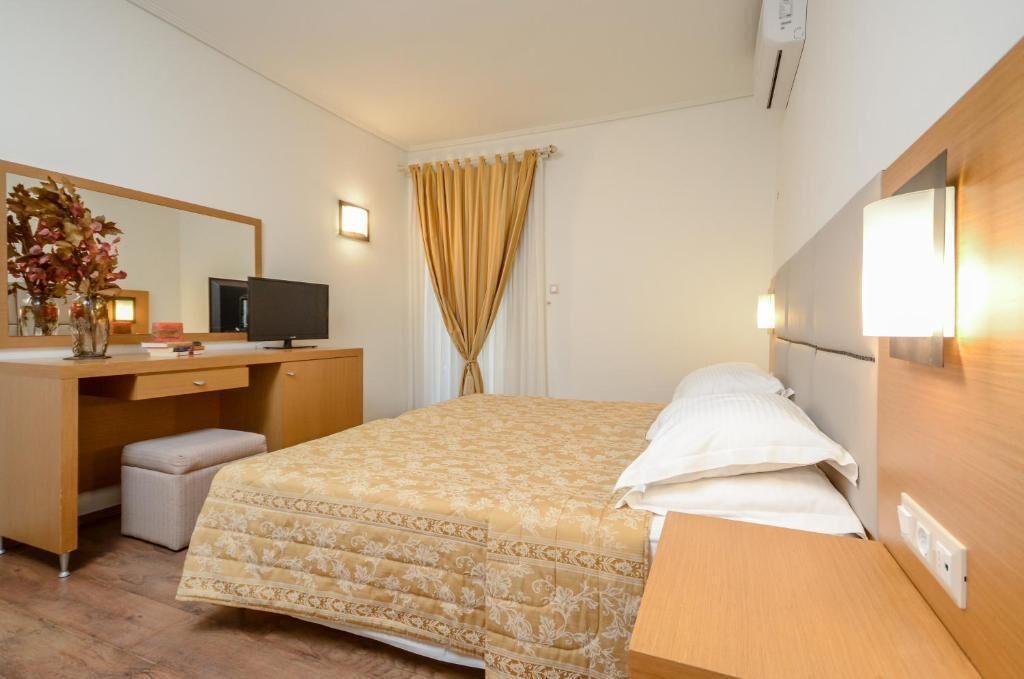 A hotel room with a bed, a desk with a computer, a mirror, and a window with curtains.